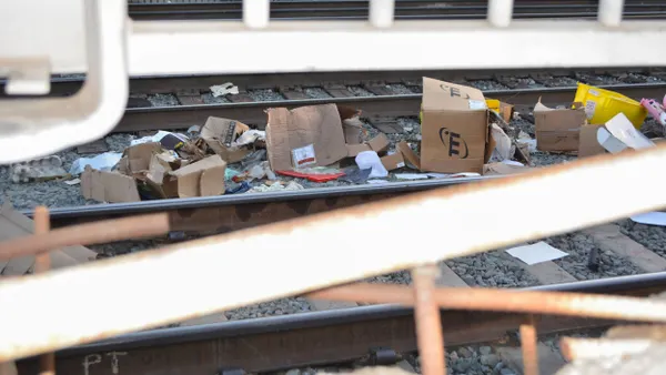 Open packages and debris on railroad tracks is seen through metal fencing.