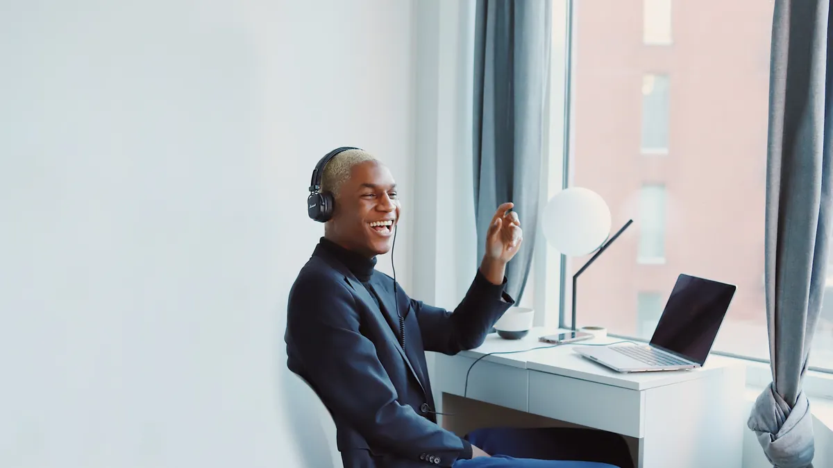 A Black person in a headset laughs while working from home