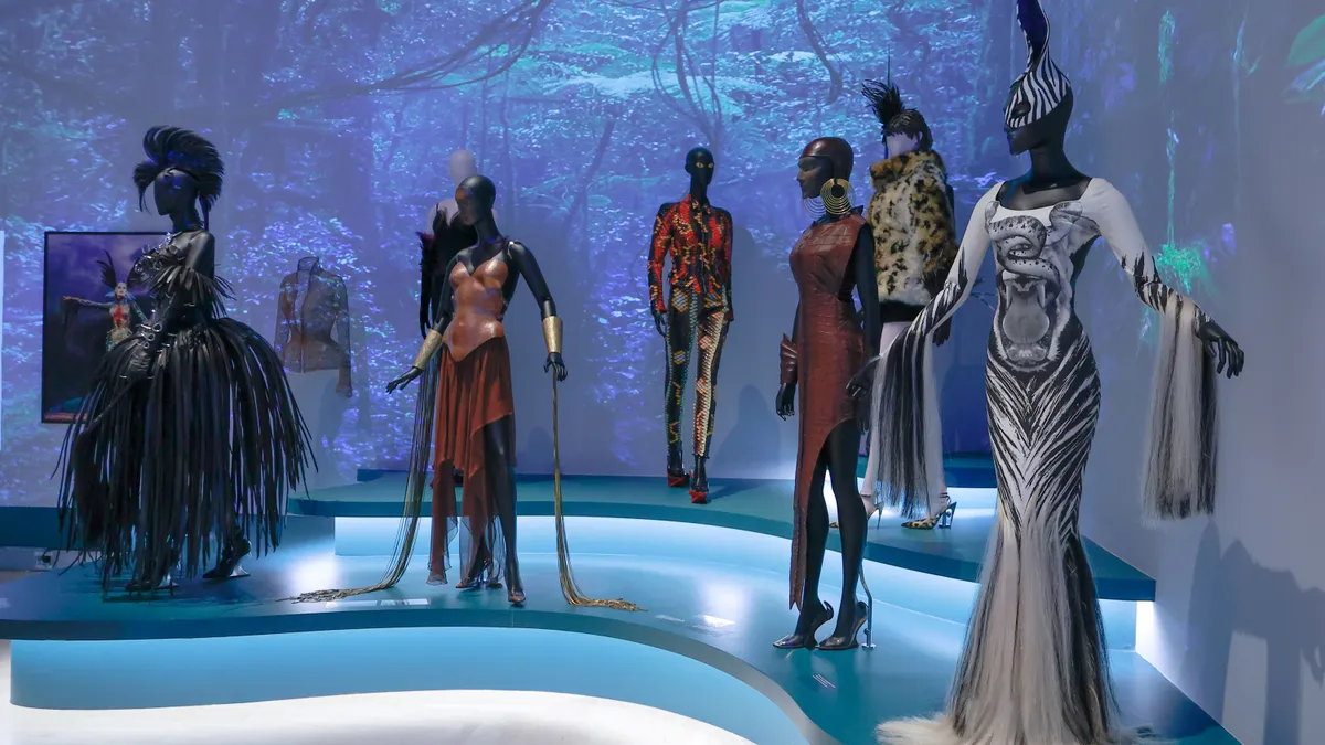 Mannequins display archival dresses from designer Thierry Mugler on a blue lit stage.