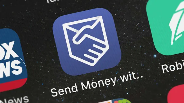 Close-up of a smartphone screen showing an app icon with a blue background and a handshake logo inside a stylized envelope. The text below reads "Send Money wit..".