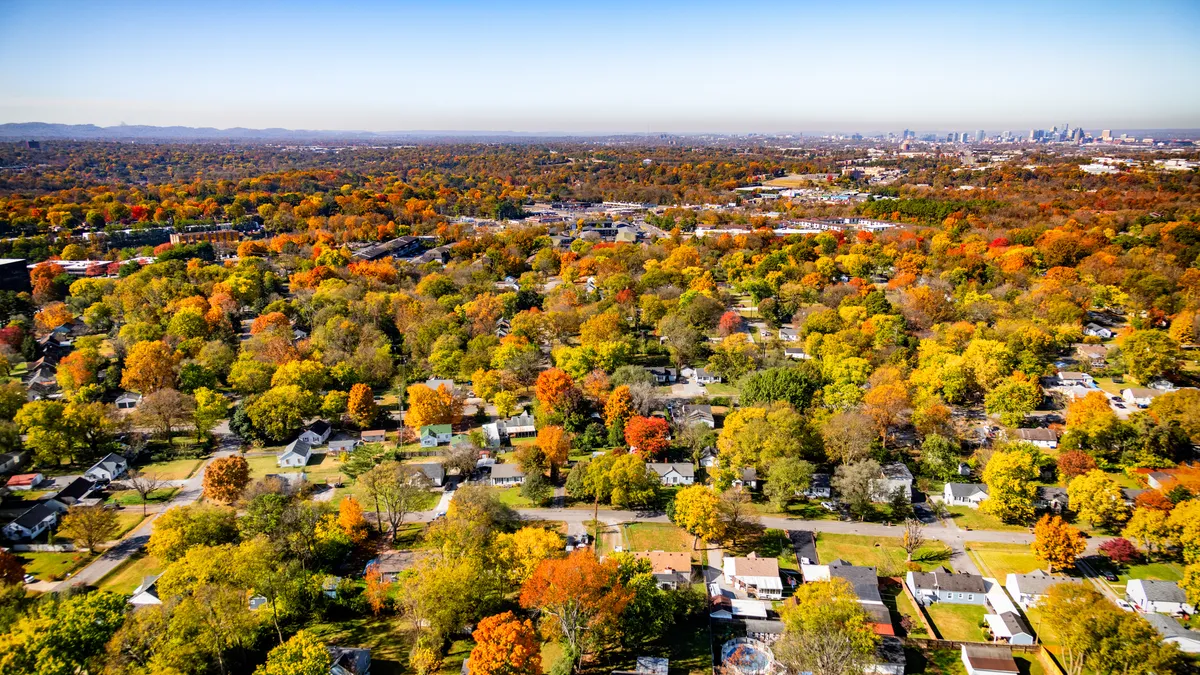 Suburban neighborhood with houses and trees in foreground, Nashville skyline background