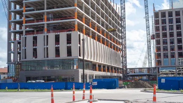 Construction site with cone yard sign, high-rise hotels, office building, skyscraper structure, working cranes, lower floor precast concrete wall in downtown Irving, Texas, commercial real estate