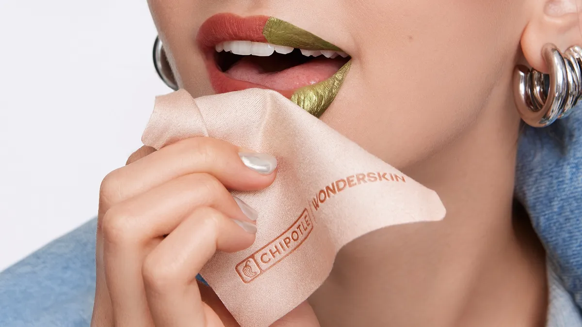 A person wearing lip stain holds a Chipotle x Wonderskin napkin