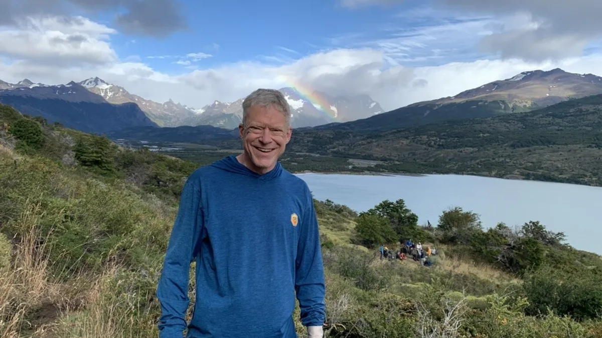 A person in hiking gear stands for a photograph with mountains in the background.