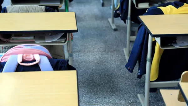 Rows of desk sit empty with backpacks and jackets sitting on the back of nearby chairs.
