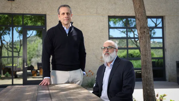A person stands next to a table where another person sits.