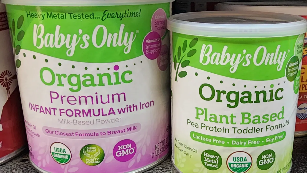 A purple can and a green can of Nature's one Baby's Only organic infant formula brand on a store shelf.