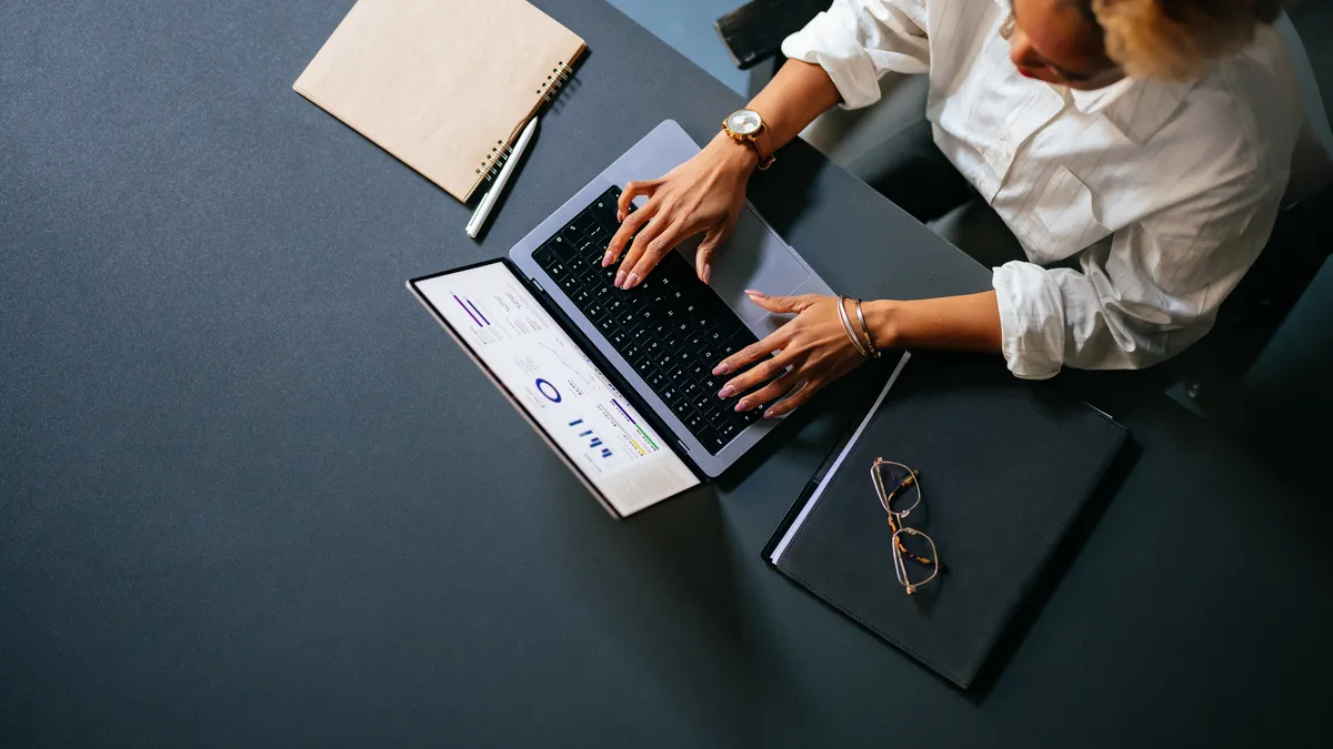 High angle view of person working on a laptop computer with notes and glasses nearby