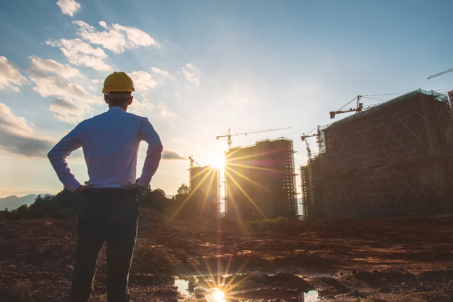 a man in a hard hat looks over a construction site as the sun goes down