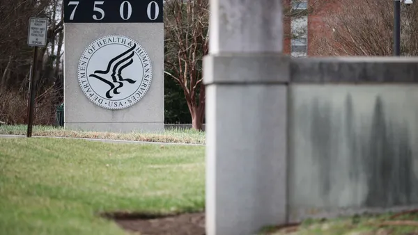 A concrete sign outside of a building reads "Department of Health & Human Services" wrapped around the HHS logo.
