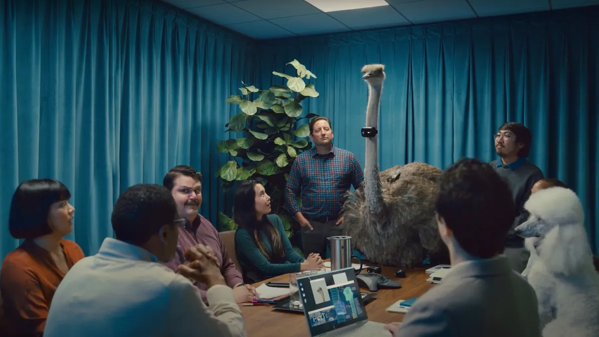 A group of businesspeople sit in a conference room gathered around an ostrich wearing an imaginary device that translates animal speech.