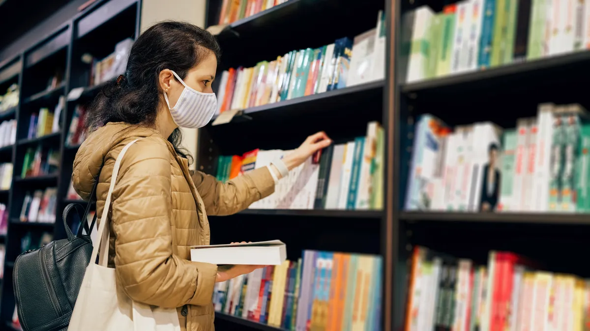 Woman with protective face mask reading a book in the bookstore.