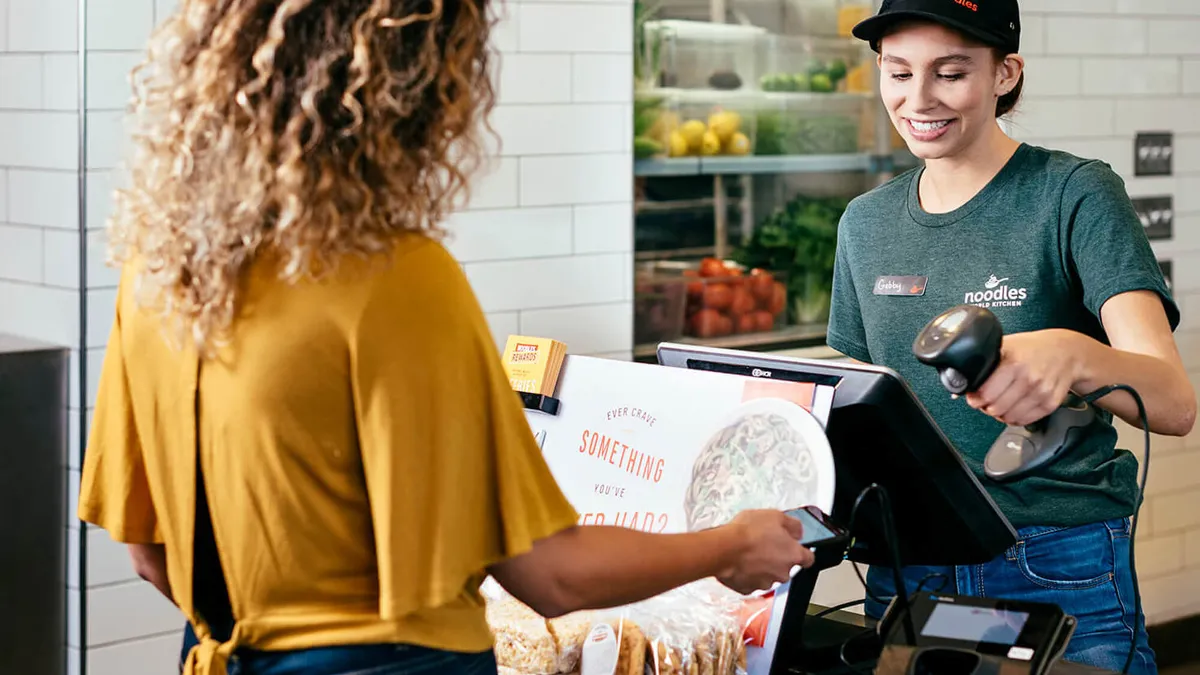 An image of a customer showing a smartphone to a Noodles & Company cashier