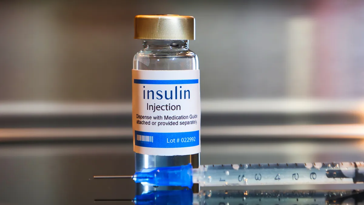 A vial of insulin and a needle on a table