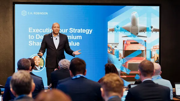 A crowd sits in chairs in front of tables and computers while listening to C.H. Robinson President and CEO Dave Bozeman present for a company investment event.