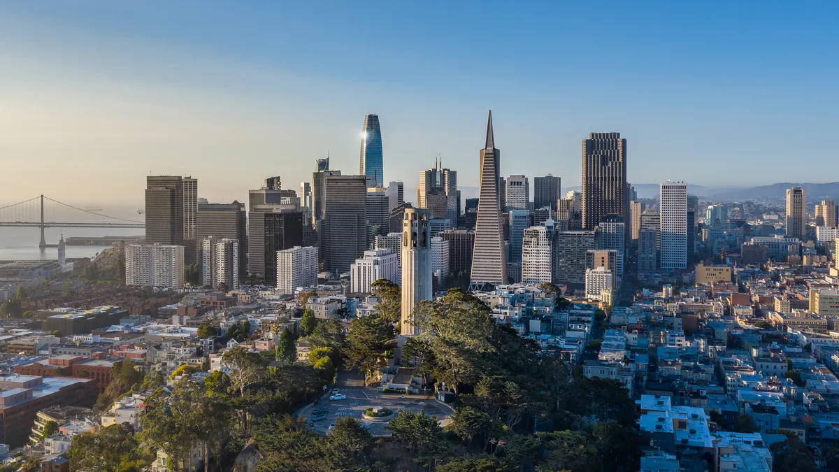 An aerial view on a sunny morning of several of San Francisco's most well known architectural landmarks. A backdrop of the skyscrapers and Bay Bridge behind them.