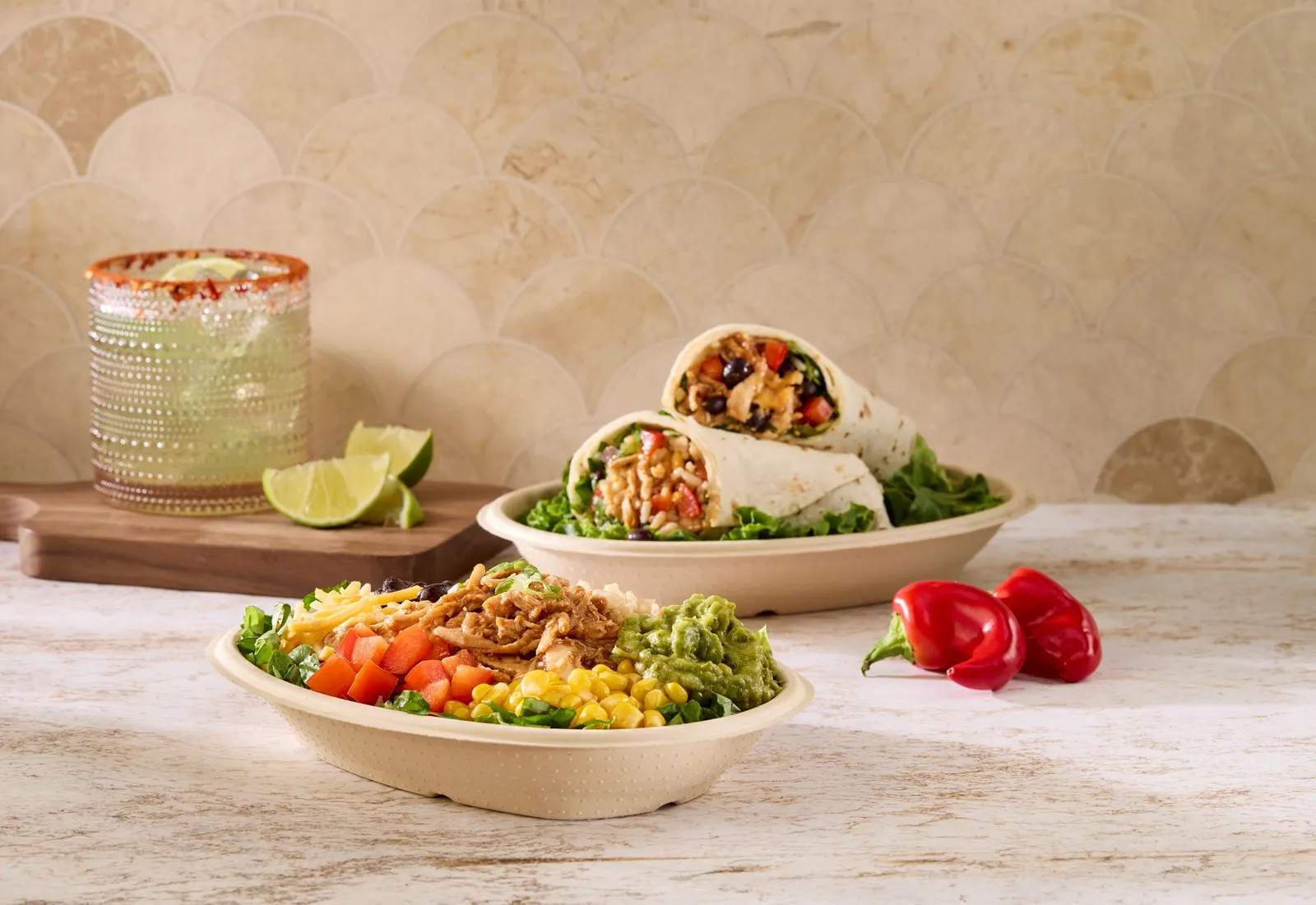 A molded fiber bowl containing salad. sits on a counter next to a molded fiber container holding a burrito.