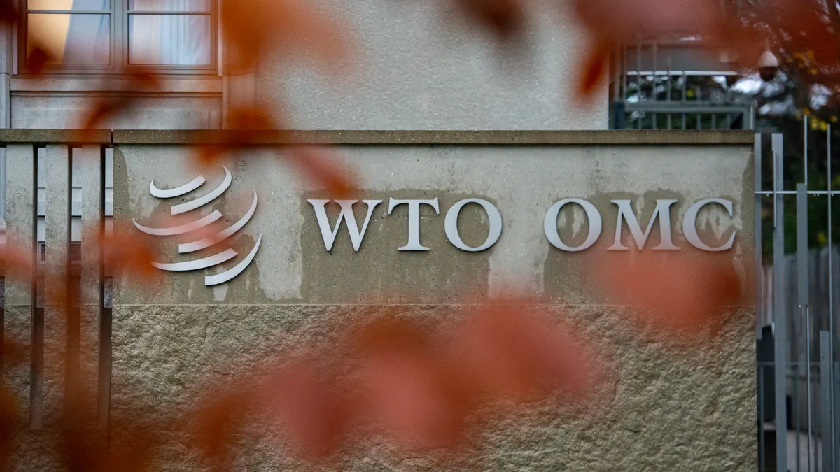 A sign reading "WTO OMC" is seen with fall foliage around it.