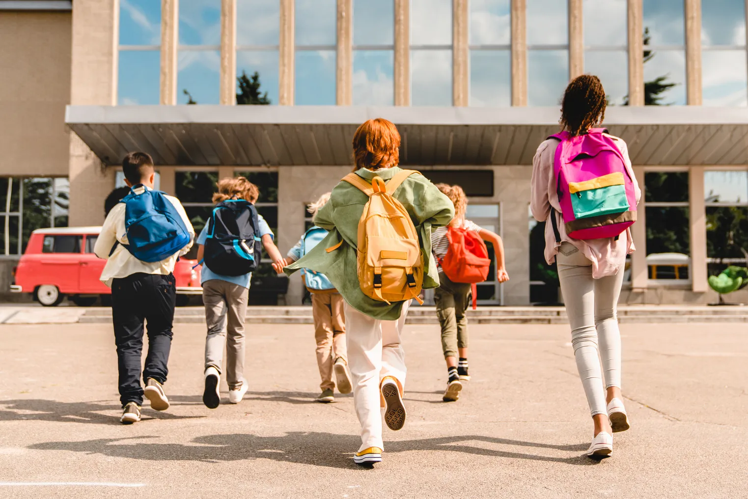 School children with backpacks running toward a school building.