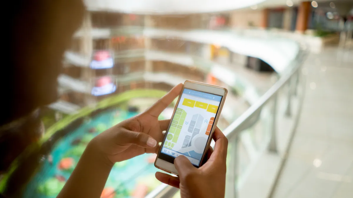 A close-up shot of a woman using an app on her cell phone with the map of a shopping mall.