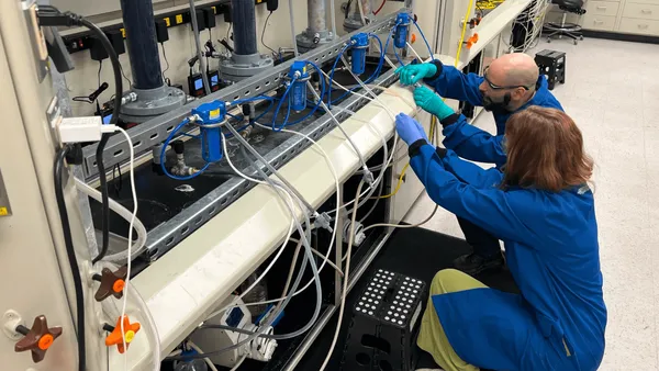 Two people in safety suits kneel in front of a machine with tubes