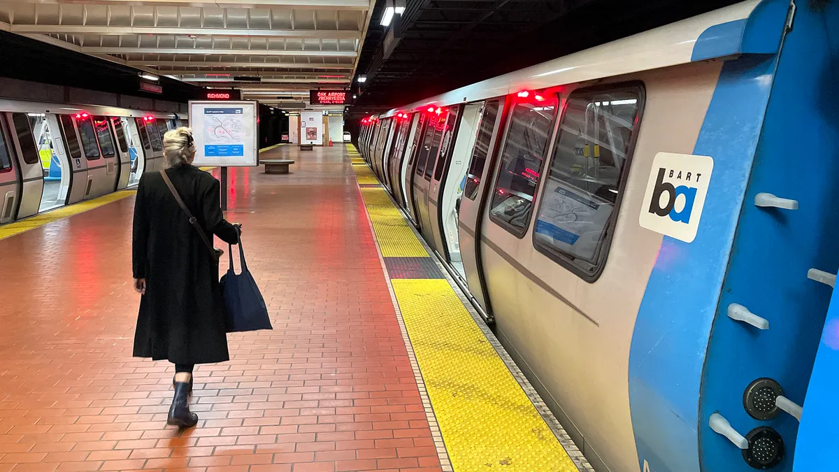 A lone woman on the platform at the North Berkeley station with two Bay Area Rapid Transit trains stopped with their doors open.