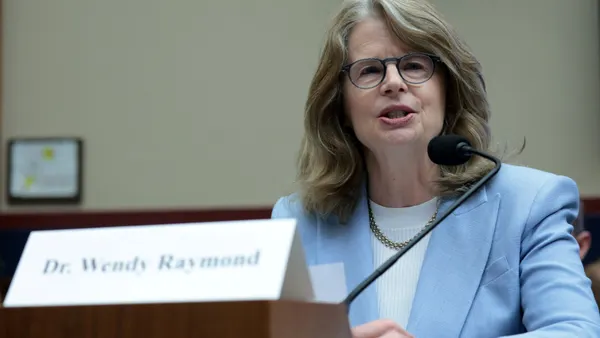 Wendy Raymond speaks into a microphone at a desk.