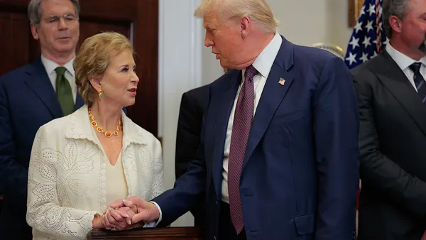 Two people are standing side by side and shaking hands inside a room.