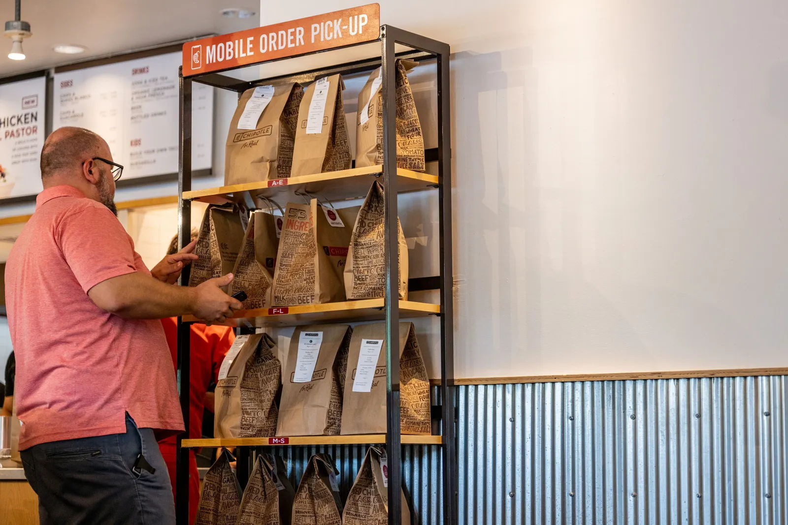 A person stands in front of shelves that contain several paper bags with food in them,