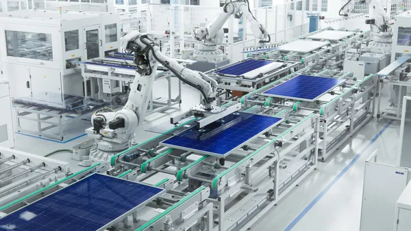 A wide shot of a solar panel production line with robot arms in a factory.