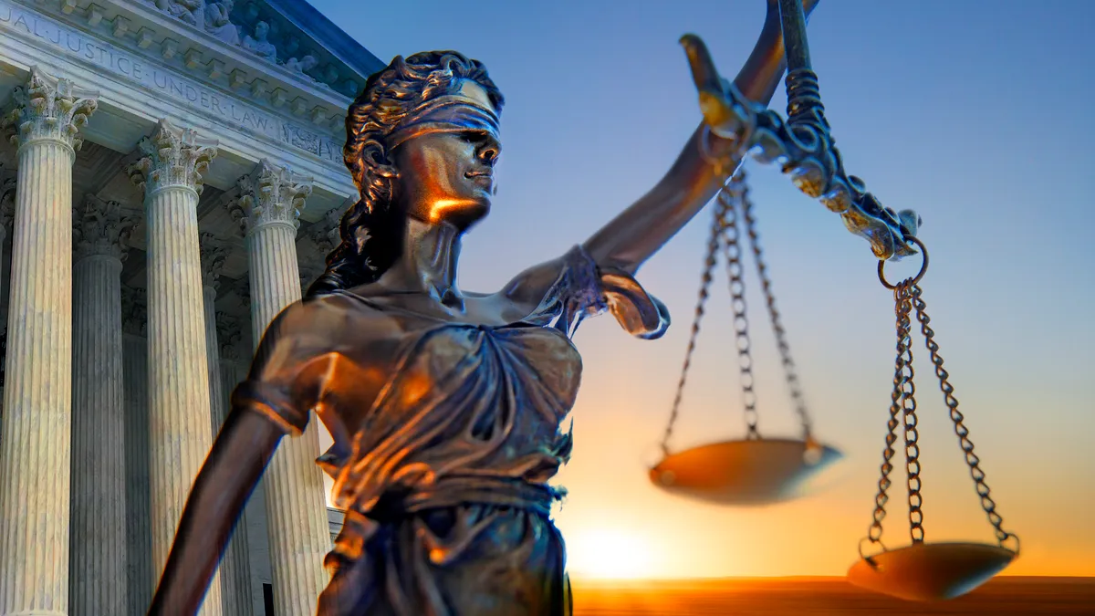 A statue of the blindfolded lady justice in front of the United States Supreme Court building as the sun rises in the distance.