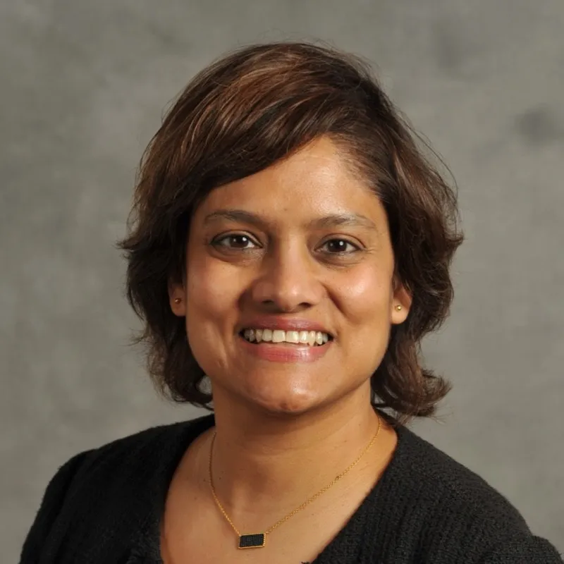 A corporate headshot of a woman in a black sweater against a gray background