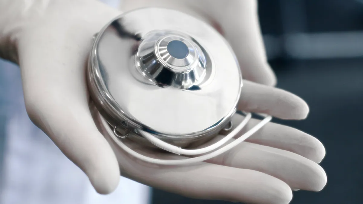 A person wearing gloves holds a round, metallic device in their palms.