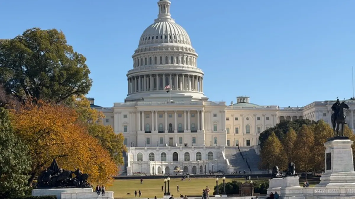 The facade of the U.S. Capitol building is seen along with trees and a reflection pond