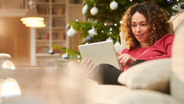 A woman browses an ecommerce site in front of a Christmas tree.