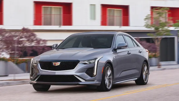 A dark gray 2021 Cadillac CT4 sedan parked in front of a white multi-story apartment building with red accents.