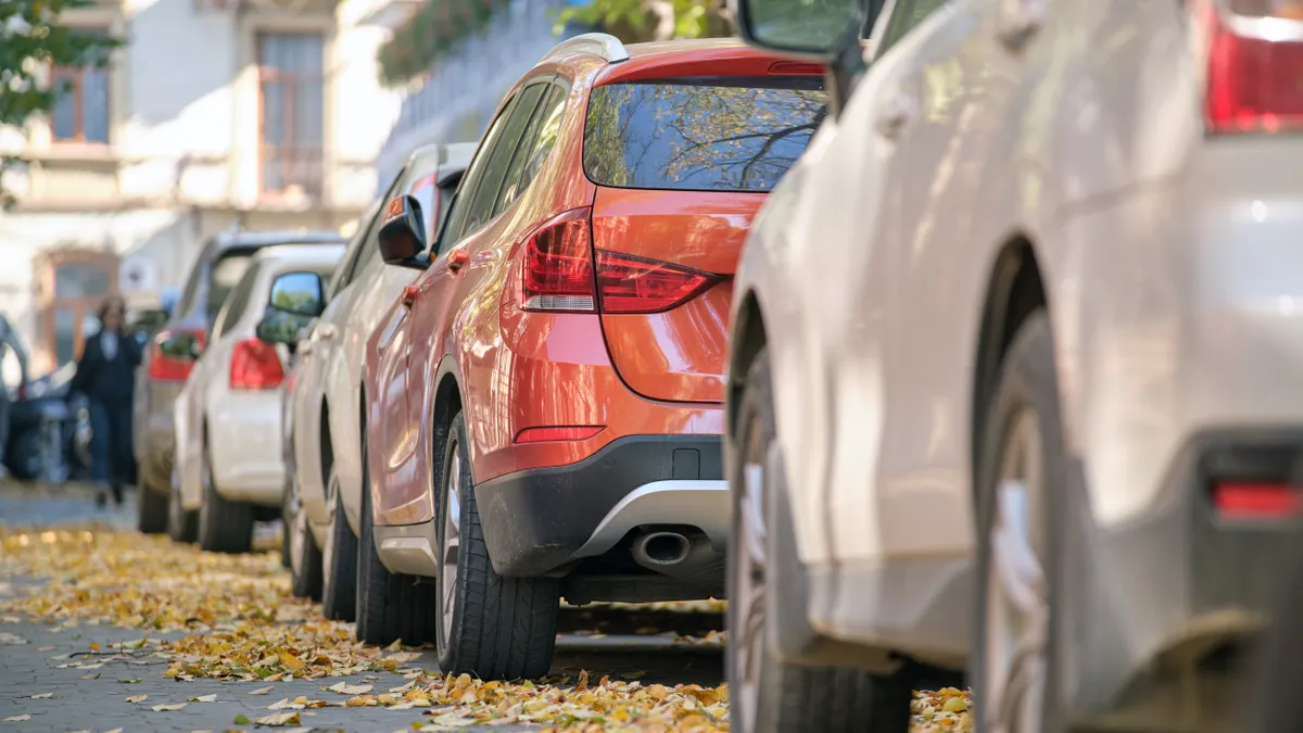 A low angle view of a street lined with parked cars with buildings in the background and autumn leaves on the street.