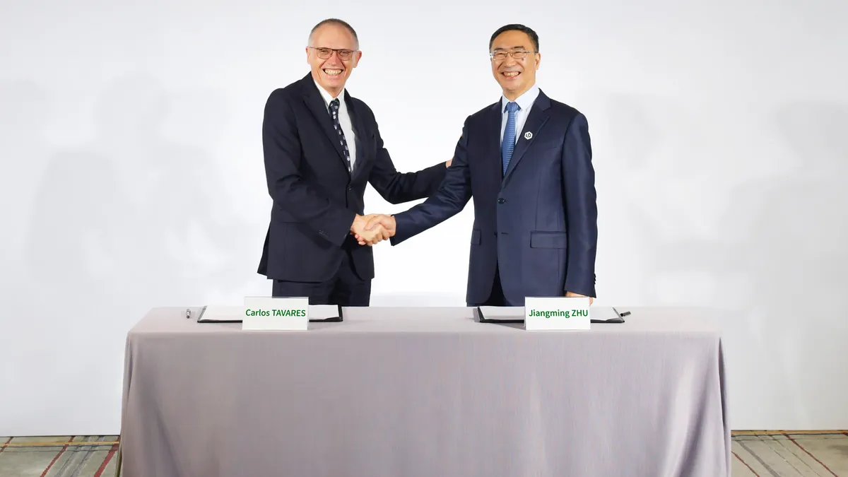 Stellantis CEO Carlos Tavares shakes hands with Leapmotor CEO Zhu Jiangming behind a table at a strategic cooperation signing ceremony.