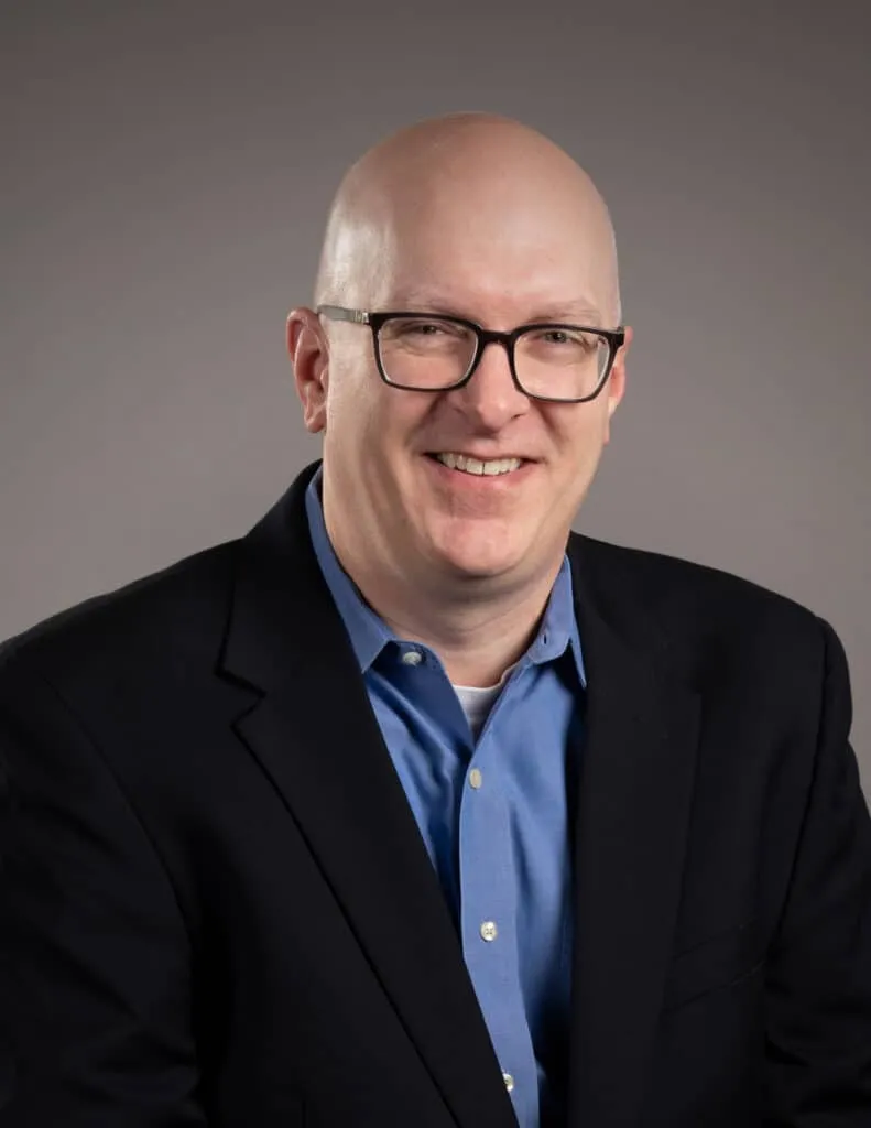 Headshot of white male in a black blazer and blue button down