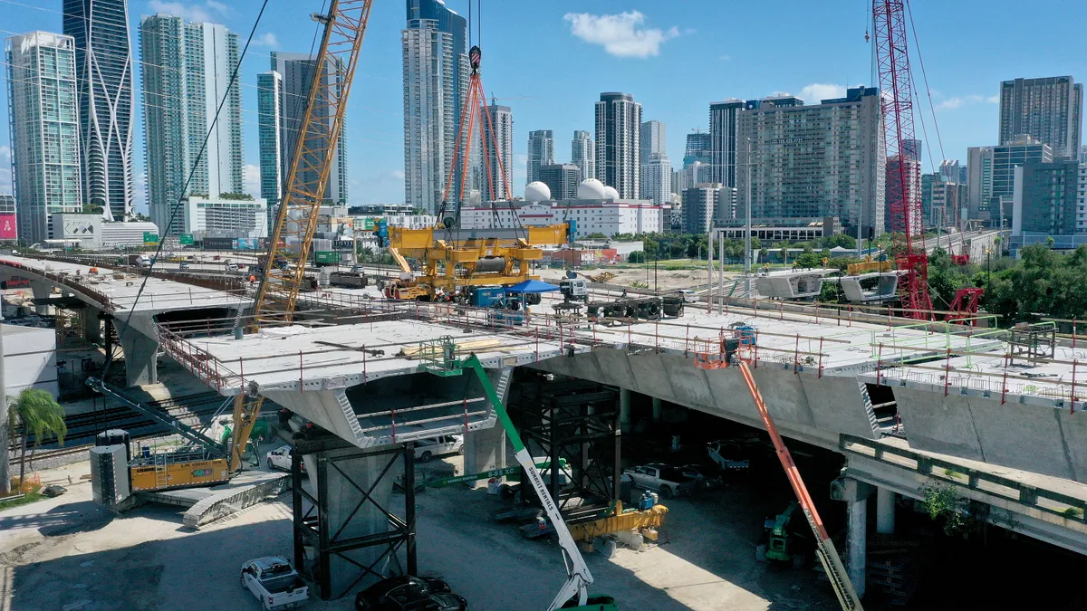 Aerial view of a construction equipment on and around an elevated double highway bridge with an urban skyline in the background.