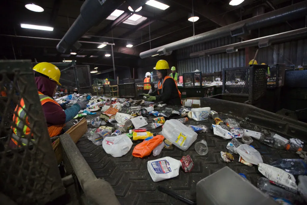 Workers in safety gear sort recyclables on a conveyor belt