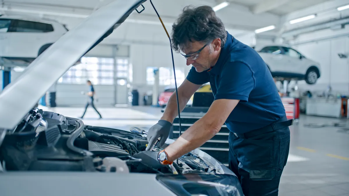 Male mechanic works on a car engine at an auto repair shop.