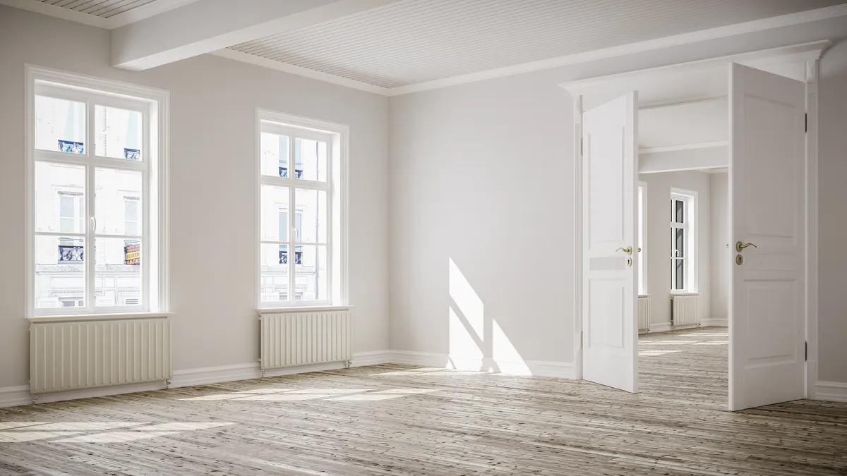 An empty white room with two windows and a pair of French doors leading into another room.