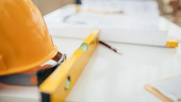 A photo of a hard hat, construction plans and tools on a table.