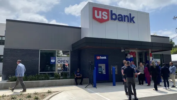 A U.S. Bank branch is shown with a small crowd of people standing near the front entrance. A sign in the window of the building says "Now Open."