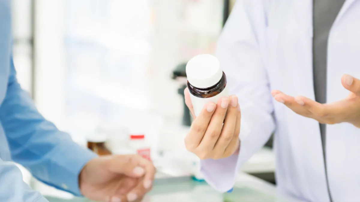 Female pharmacist holding medicine bottle giving advice to customer in chemist shop or pharmacy