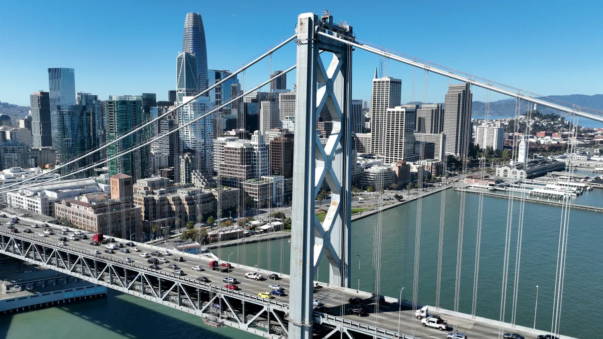 In an aerial view, cars drive by the San Francisco skyline as they cross the San Francisco-Oakland Bay Bridge