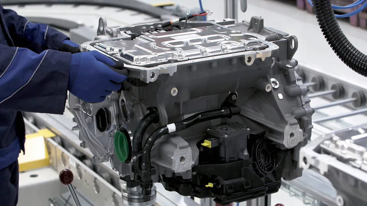 An factory worker with an electric car motor on an assembly line.