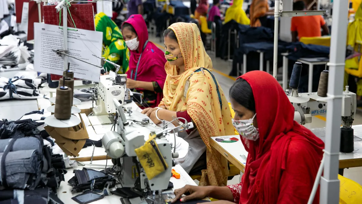 Three people work on garments in Bangladesh side by side on sewing machines.