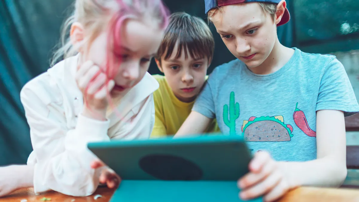 Three children playing games at digital tablet.